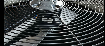 a close up of a fan with a grey metal grate at the top of an air conditioning unit outside