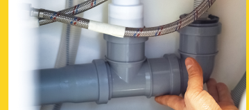 a grey pvc pipe is connected to existing hoses under a sink