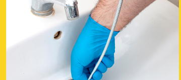 someone wearing a blue glove and inserting a coiled tool into a drain